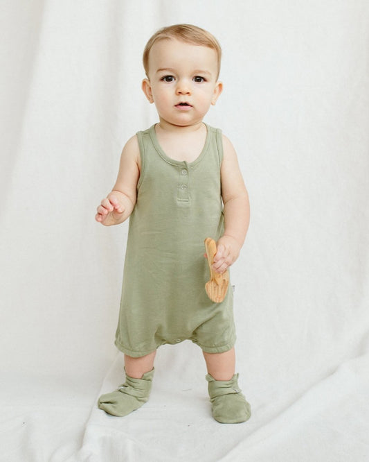 Baby wearing a green romper holding a wooden toy on a white background