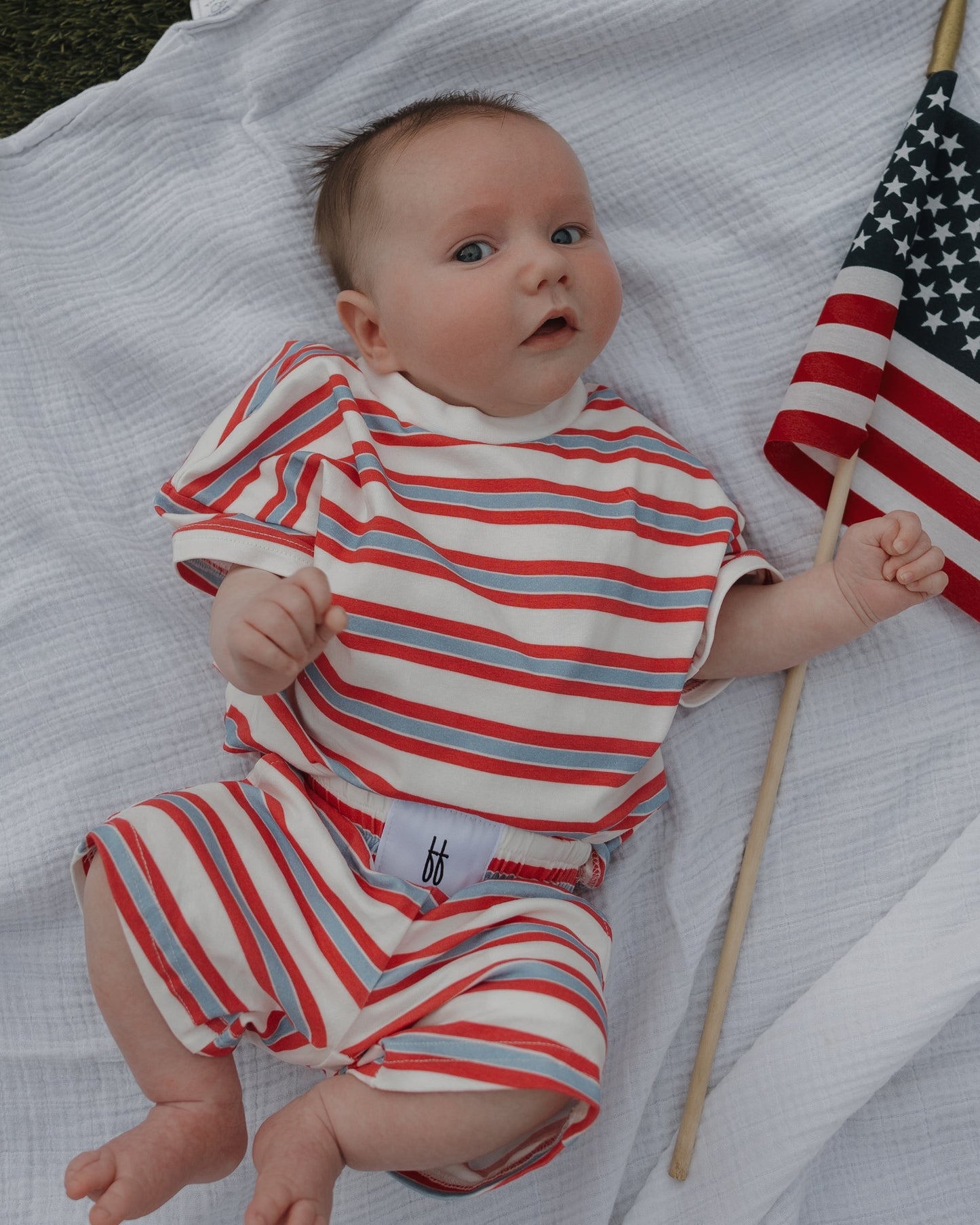 Baby in a red, white, and blue striped outfit holding an American flag.