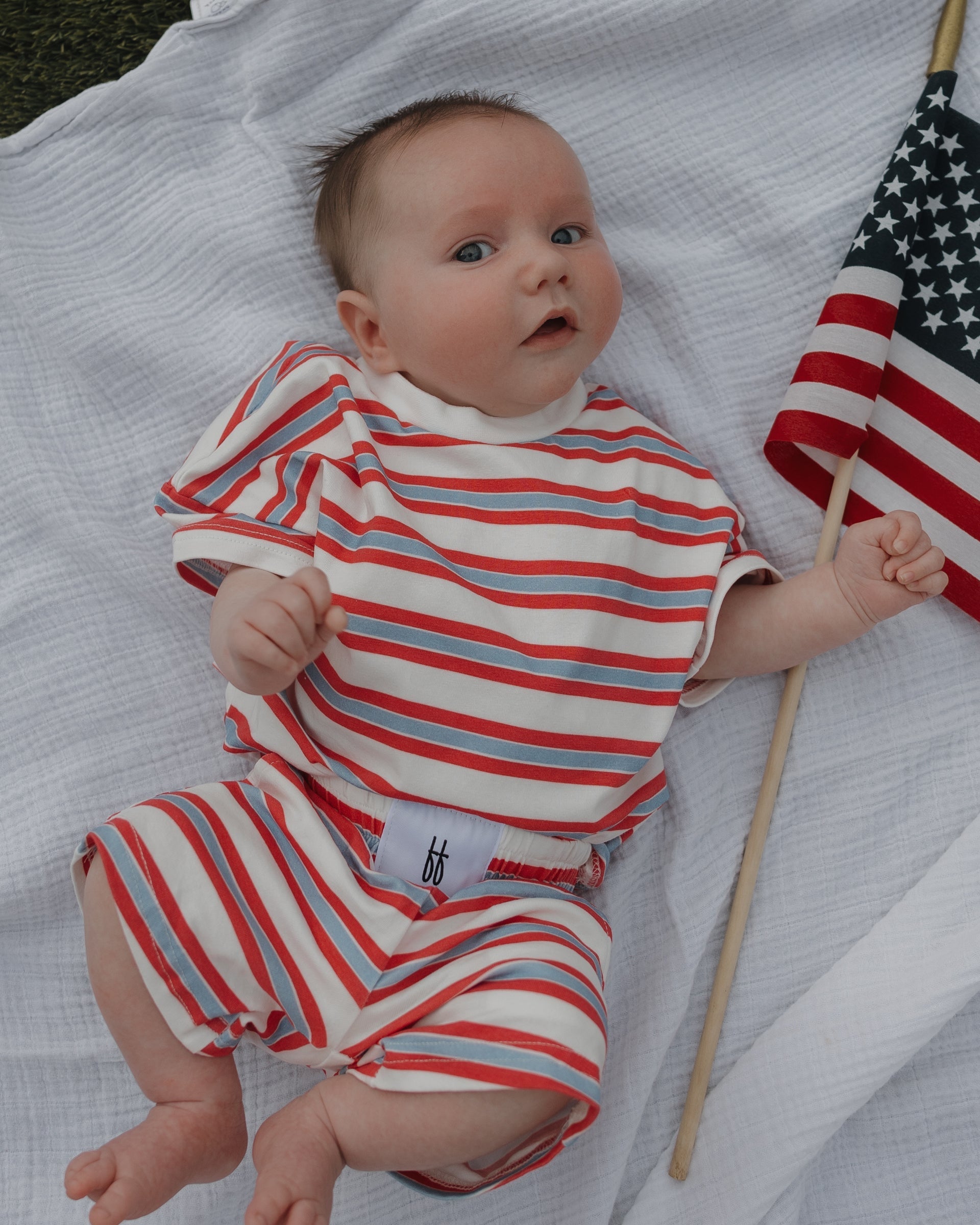 Baby in a red, white, and blue striped outfit holding an American flag.