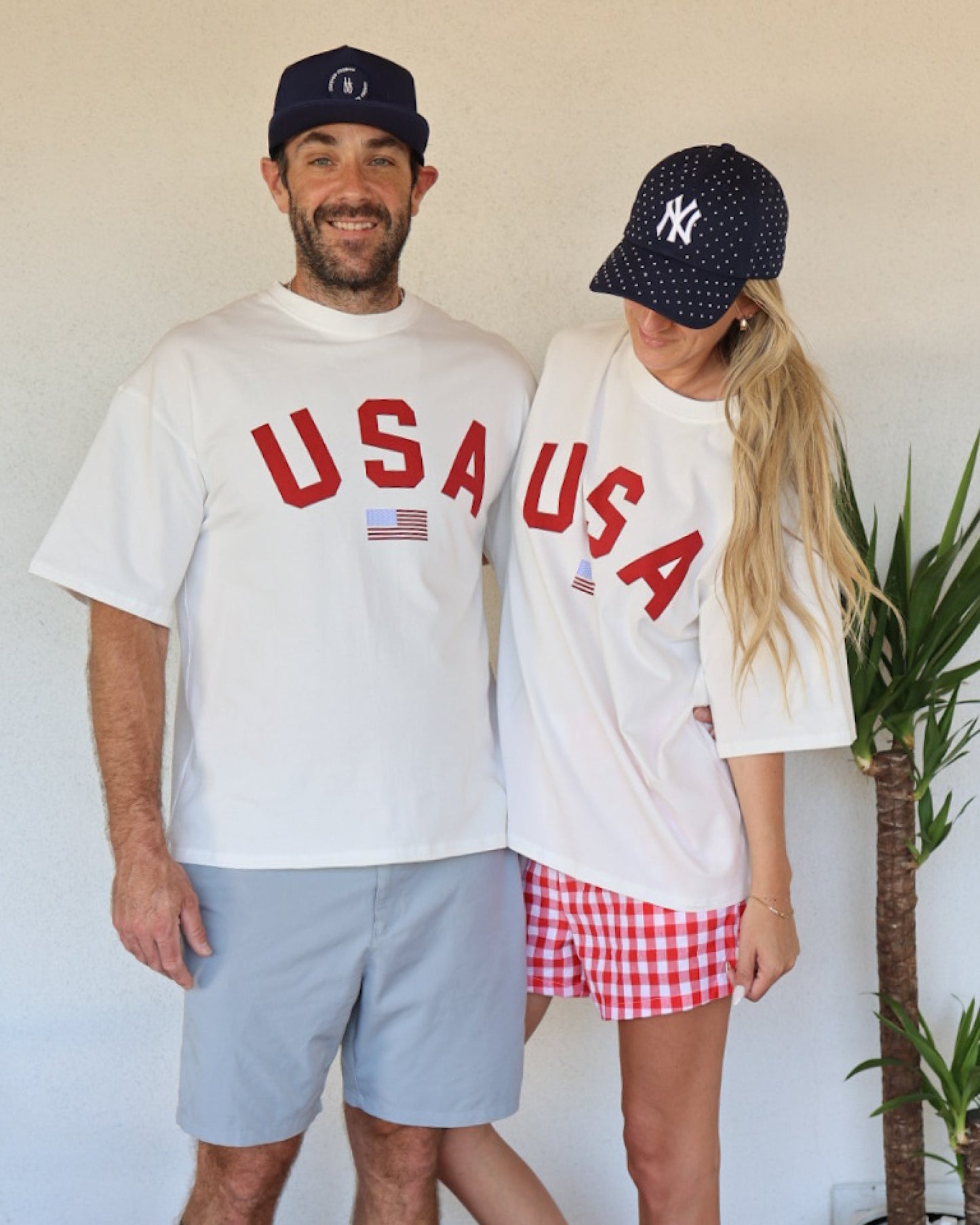 Two people wearing 'USA' t-shirts and baseball caps standing next to each other.
