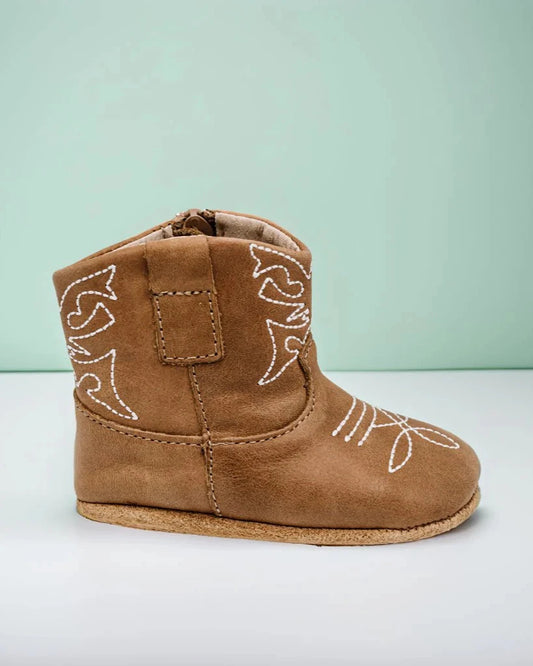 Brown baby boot with white stitching on a light green background