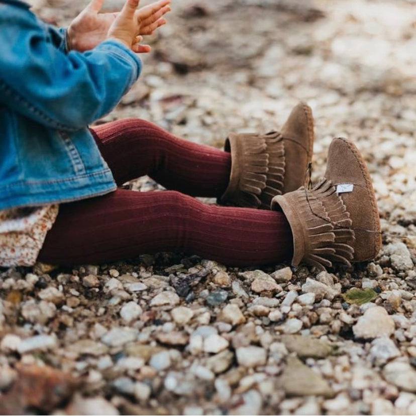 Person wearing brown fringed boots sitting on a rocky ground.