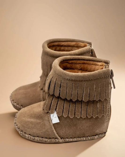 Pair of brown suede boots with fringes on a beige background