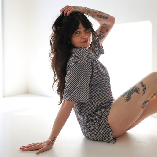 Woman in a checkered outfit sitting on a white surface with a bright light source behind her.